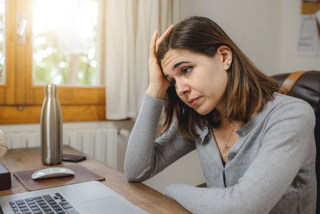 A woman looking at a laptop. She looks burnout and exhausted.