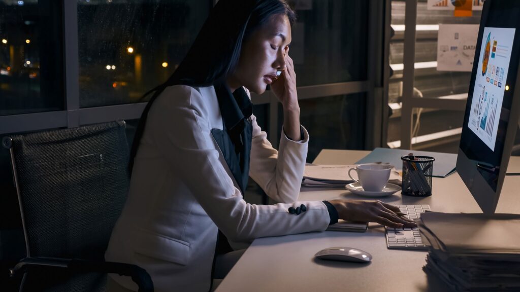 A woman sits at her desk late at night looking tired